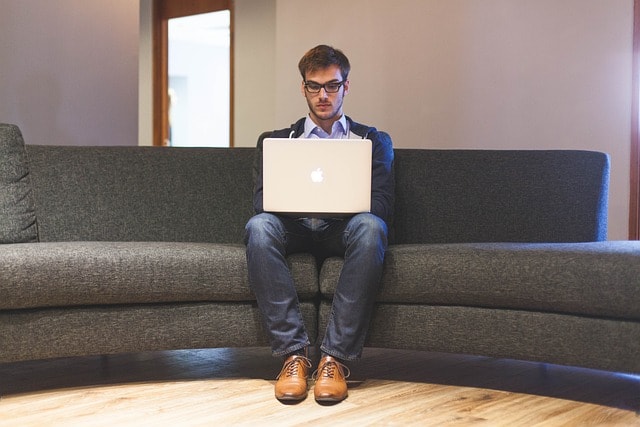 A man sitting on a couch and working on a laptop.